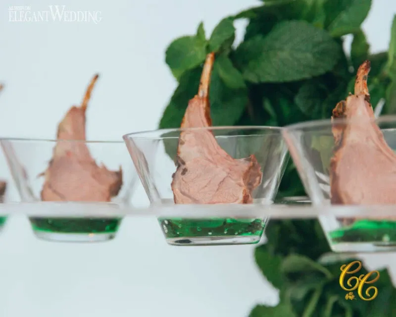 This image features a visually appealing presentation of lamb chops elegantly served in clear glass bowls. Each bowl is filled with a vibrant green sauce, adding a touch of sophistication to the dish. The background showcases lush green foliage, enhancing the fresh and elegant atmosphere. This image highlights the culinary offering of C’est Classique, a renowned wedding venue under the category of Wedding Venues at Mariage Elegant, Canada, known for its exquisite cuisine and attention to detail.