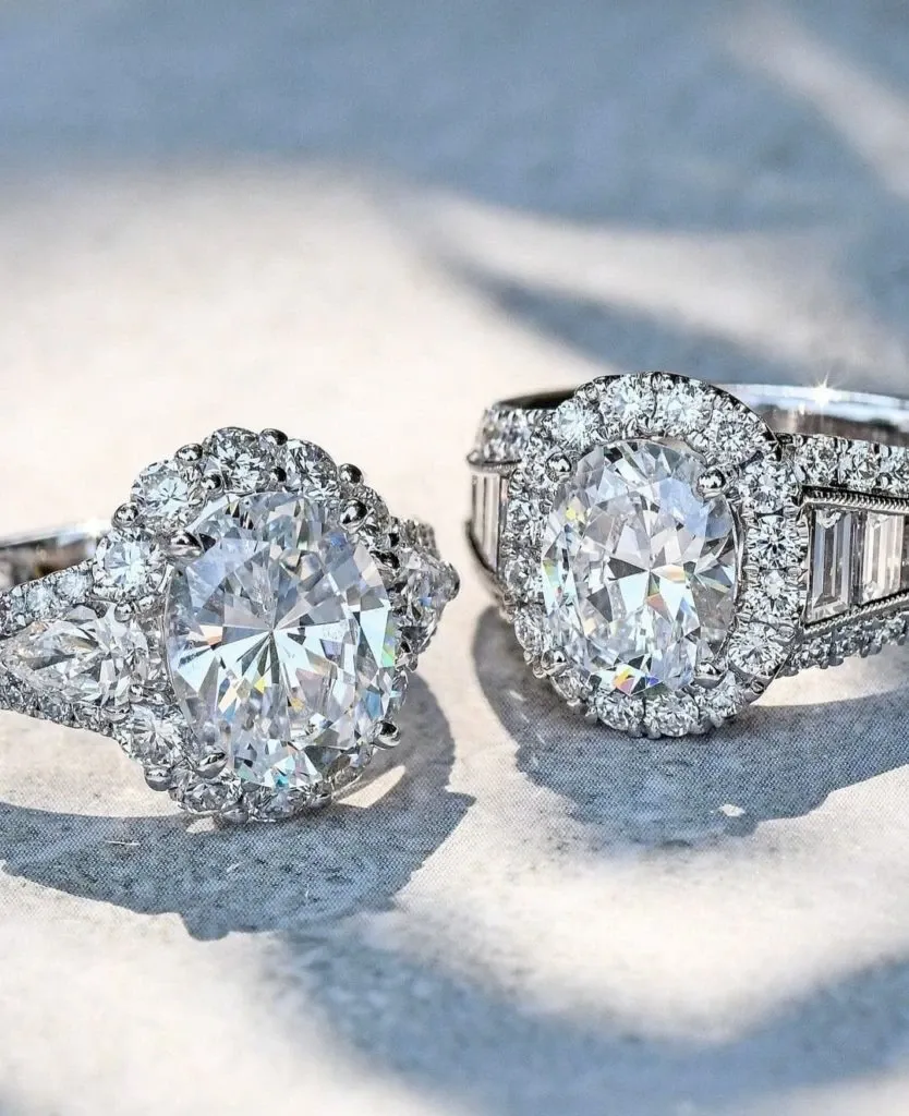 Exquisite wedding jewelry by Bijouterie B. Serkos featuring two stunning diamond rings displayed on a soft, neutral fabric background. The left ring showcases a brilliant round center diamond encircled by a halo of smaller diamonds, enhancing its sparkle. The right ring features a captivating oval diamond surrounded by a delicate halo of diamonds and accentuated with baguette-cut diamonds along the band. These elegant pieces exemplify luxury and craftsmanship, ideal for weddings, embodying the sophistication and beauty sought by couples at Mariage Elegant in Canada.