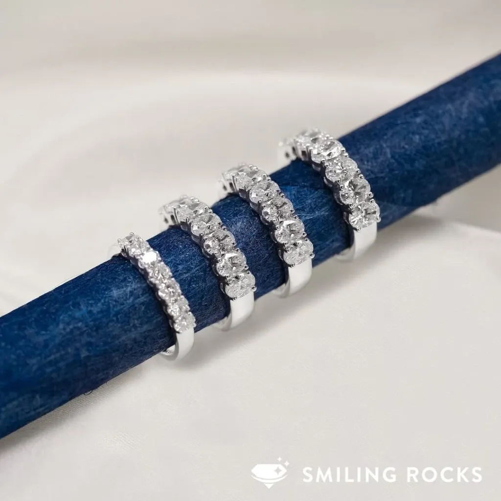 Four elegant silver wedding bands, each adorned with a row of sparkling diamonds, are displayed on a plush, blue velvet roll. The jewelry showcases the exquisite craftsmanship of Bijouterie B. Serkos, fitting perfectly within the wedding jewelry category. This image highlights the sophisticated and timeless appeal of the rings, ideal for any couple planning their nuptials through Mariage Elegant in Canada.