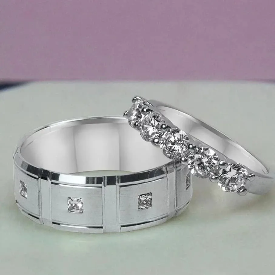 The image features two exquisite wedding rings from Bijouterie B. Serkos, a vendor in the wedding jewelry category. The first ring is a sleek, wide band adorned with small, evenly spaced square diamonds embedded in a polished silver band, showcasing a modern design. The second ring is a delicate, silver band set with a row of brilliant round-cut diamonds, adding an elegant sparkle. These rings are perfect for couples seeking both contemporary and classic styles for their wedding jewelry, underlining Bijouterie B. Serkos's commitment to quality and craftsmanship.