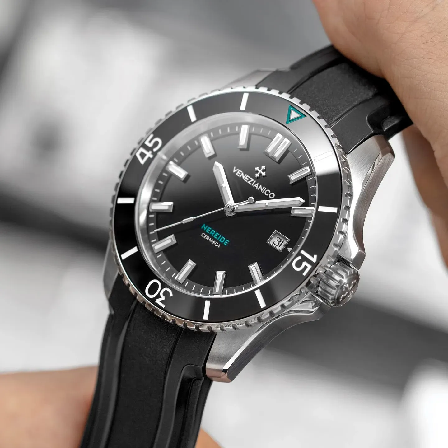 A luxurious silver wristwatch with a black bezel and black rubber strap from Bijouterie La Voûte is displayed prominently. The watch face features bold silver hour markers and hands, with a date display at the 3 o'clock position. This elegant timepiece fits perfectly within the wedding jewelry category, offering a sophisticated accessory option for grooms or groomsmen. The design emphasizes both style and functionality, making it an ideal choice for special occasions like weddings, where attention to detail is paramount. The background is blurred, keeping focus on the watch and its intricate design features.