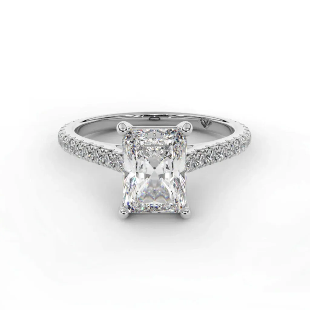 A stunning engagement ring from Bijouterie La Voûte, showcased in the Wedding Jewelry category for Mariage Elegant, Canada. The image features a radiant-cut diamond set in a classic four-prong setting. The band is elegantly adorned with a row of small sparkling diamonds, enhancing the ring's sophisticated and luxurious appeal. This exquisite piece is ideal for couples seeking timeless elegance in their wedding jewelry selection.