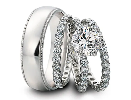 A stunning display of wedding jewelry by Eternal Diamonds, featuring a trio of elegant rings. The set includes a classic men's wedding band with a sleek, polished silver finish, complemented by two intricately designed women's rings. Each women's ring is adorned with a series of sparkling diamonds, with one showcasing a prominent round-cut diamond as its centerpiece. This exquisite collection perfectly embodies sophistication and luxury, ideal for couples in Canada planning their special day through Mariage Elegant.