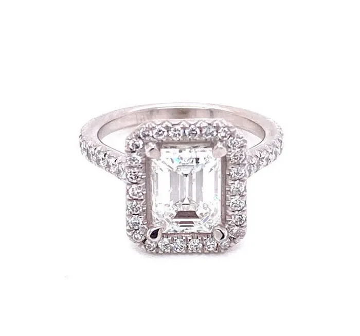 The image features a stunning emerald-cut diamond engagement ring by Eternal Diamonds, categorized under wedding jewelry for Mariage Elegant in Canada. The centerpiece is an exquisite emerald-cut diamond, surrounded by a halo of smaller round diamonds that enhance its brilliance. The band is further adorned with additional small diamonds, adding an extra touch of elegance and sparkle. This luxurious piece exemplifies timeless sophistication, perfect for a glamorous wedding setting.