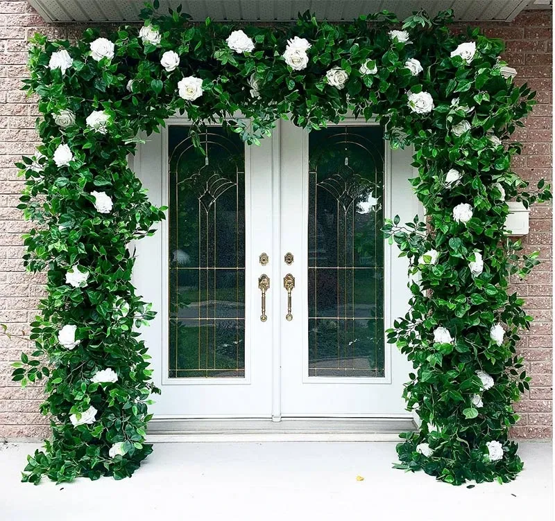 The image shows an elegant wedding decor setup by Decor and More Events, featuring a beautiful archway adorned with lush green foliage and white roses. This stylish decoration frames a set of double glass doors, creating a welcoming and romantic entrance. The floral arrangement, perfect for wedding ceremonies or receptions, showcases the vendor's expertise in transformative wedding decor, enhancing the venue's ambiance and setting the tone for an elegant event in Canada.