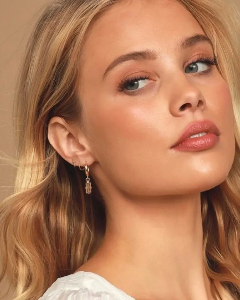 This image features a model showcasing a natural and elegant makeup look designed by Studio Caroline Théoret, a vendor in the Wedding Beauty category. The focus is on the model's flawless skin, subtle blush, and nude lipstick that together create a radiant bridal glow. Her eyes are enhanced with soft, neutral shades, highlighting the artistry suitable for weddings. She has wavy, blonde hair that cascades naturally, further adding to the refined and classic bridal style. The image exemplifies the expertise of Studio Caroline Théoret in creating timeless wedding beauty looks.
