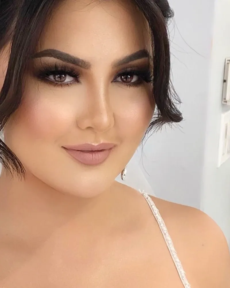 The image showcases a bride with flawless makeup, highlighting her elegant look, which is a specialty of Amber Esthetics. Her eyes are beautifully accentuated with bold, smokey eye makeup, and her lips feature a soft, natural shade. The lighting enhances her glowing skin, making her a perfect example of wedding beauty. Her hair is styled in loose, delicate waves, adding to the sophisticated bridal appearance. Amber Esthetics, known for their expertise in wedding beauty, ensures brides look stunning on their special day.