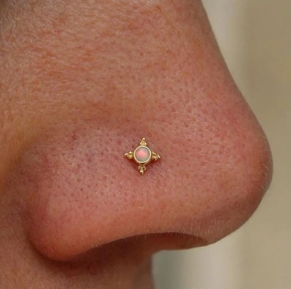 Un nez orné d'un piercing délicat en forme de carré avec une pierre rose centrale. Ce bijou fait partie des offres de Paradise Montreal, spécialisés dans la beauté pour le mariage. Le design subtil et élégant de ce piercing est parfait pour une mariée cherchant à ajouter une touche unique à son apparence le jour de son mariage.