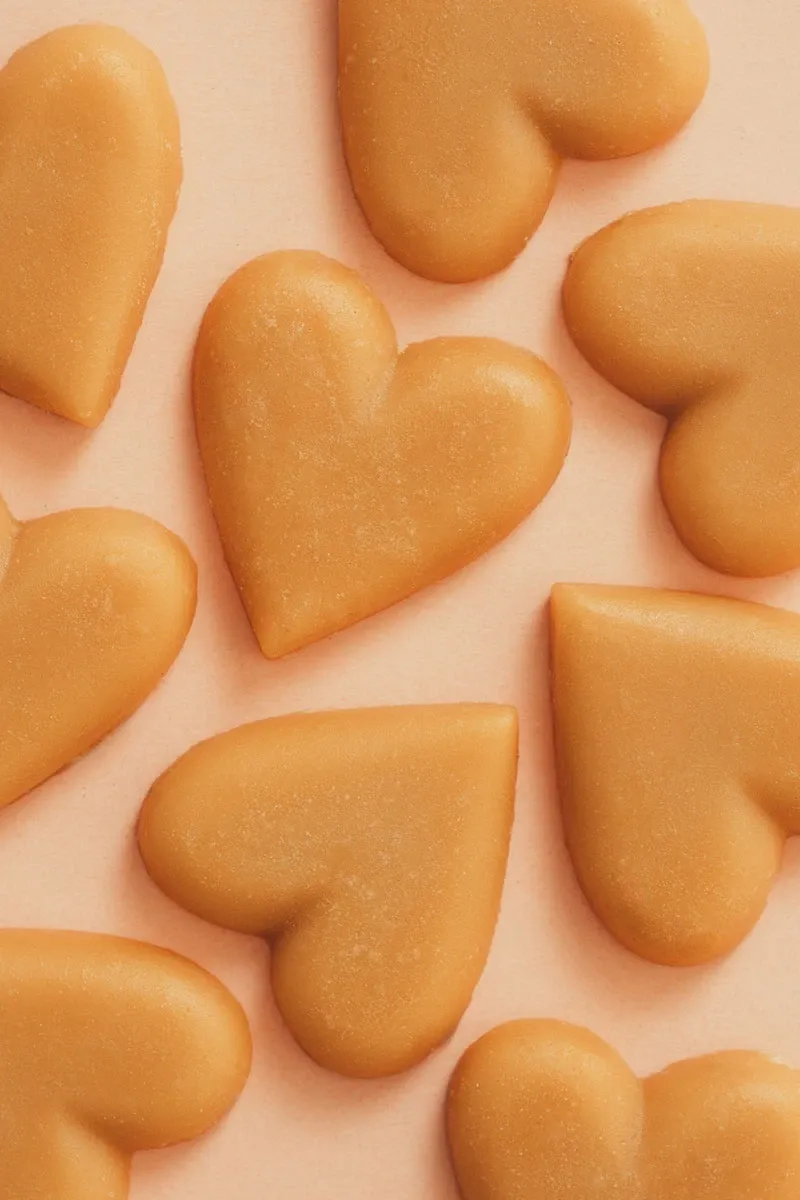 The image features a collection of heart-shaped caramel candies arranged on a soft pink background. These delightful wedding favours, with their smooth texture and rich golden-brown color, are perfect for adding a sweet touch to any celebration. Ideal for couples looking to treat their guests to a charming and tasteful gift, these candies are likely crafted by a dedicated vendor specializing in wedding confectioneries.