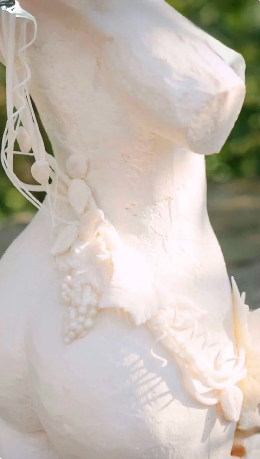 This image showcases an intricately designed wedding cake by Émotions Gâteaux, a vendor under the Wedding Cakes category on Mariage Elegant, Canada. The cake features a beautifully sculpted white horse head adorned with delicate floral and foliage details, highlighting the craftsmanship involved. The intricate sugar work includes fine lines and textures that mimic realistic features, making it a stunning centerpiece for any wedding celebration. The natural lighting emphasizes the cake's detailed artistry and elegant design, set against a soft, blurred outdoor background.