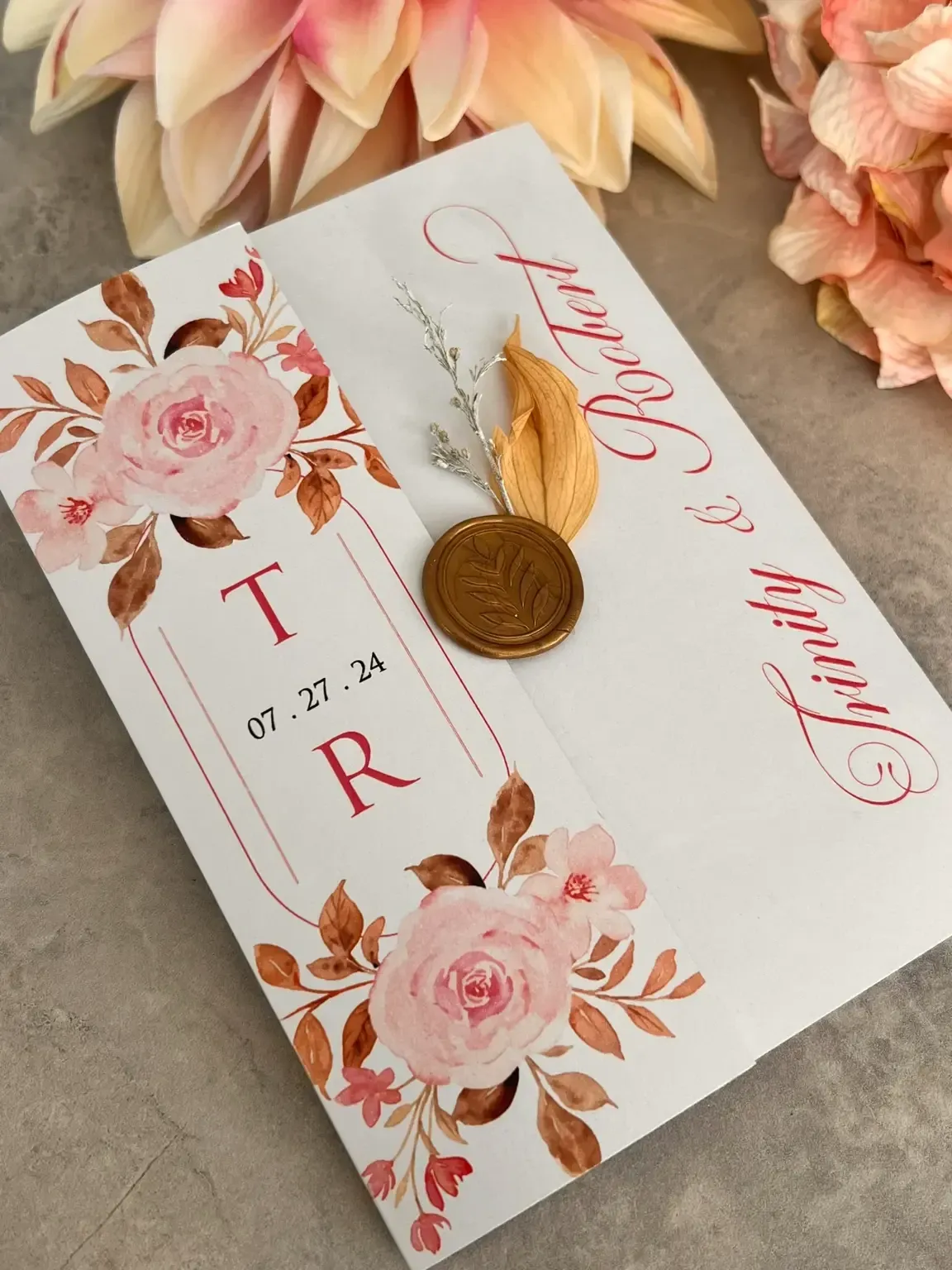 Cette image présente une invitation de mariage élégante conçue par Photogenia Design Studio, catégorie Invitations de mariage. L'invitation est ornée de magnifiques illustrations de roses roses et de feuillage délicat. Les initiales 'T R' et la date du 27 juillet 2024 sont affichées au centre. Un sceau en cire doré ajoute une touche sophistiquée. En arrière-plan, de douces fleurs pastel complètent l'esthétique romantique, idéale pour un mariage élégant.