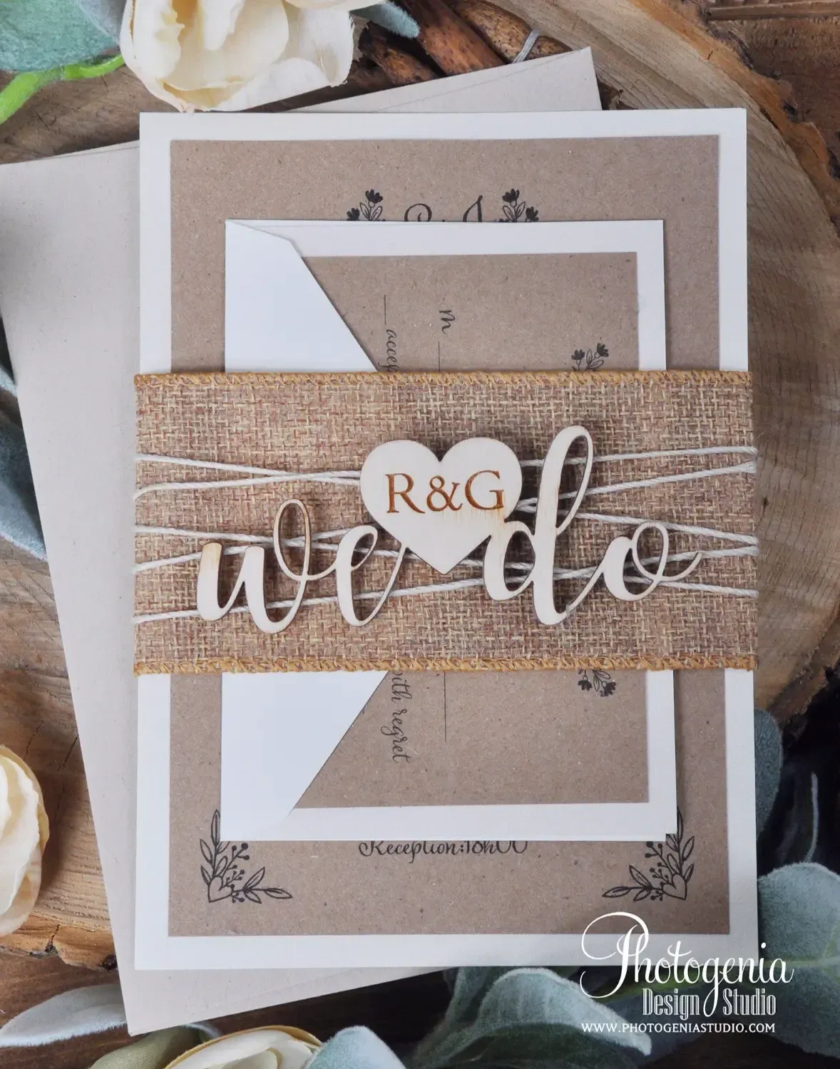 Cette image présente une invitation de mariage conçue par Photogenia Design Studio, dans la catégorie Invitations de mariage. L'invitation est ornée d'un élégant ruban de jute portant l'inscription 'we do' en lettres découpées, avec un cœur en bois marqué des initiales 'R&G'. Le design rustique-chic est complété par des enveloppes en papier kraft et des détails floraux subtils. Des fleurs blanches et crème décorent le fond, ajoutant une touche romantique et naturelle, parfaite pour un mariage élégant au Canada.