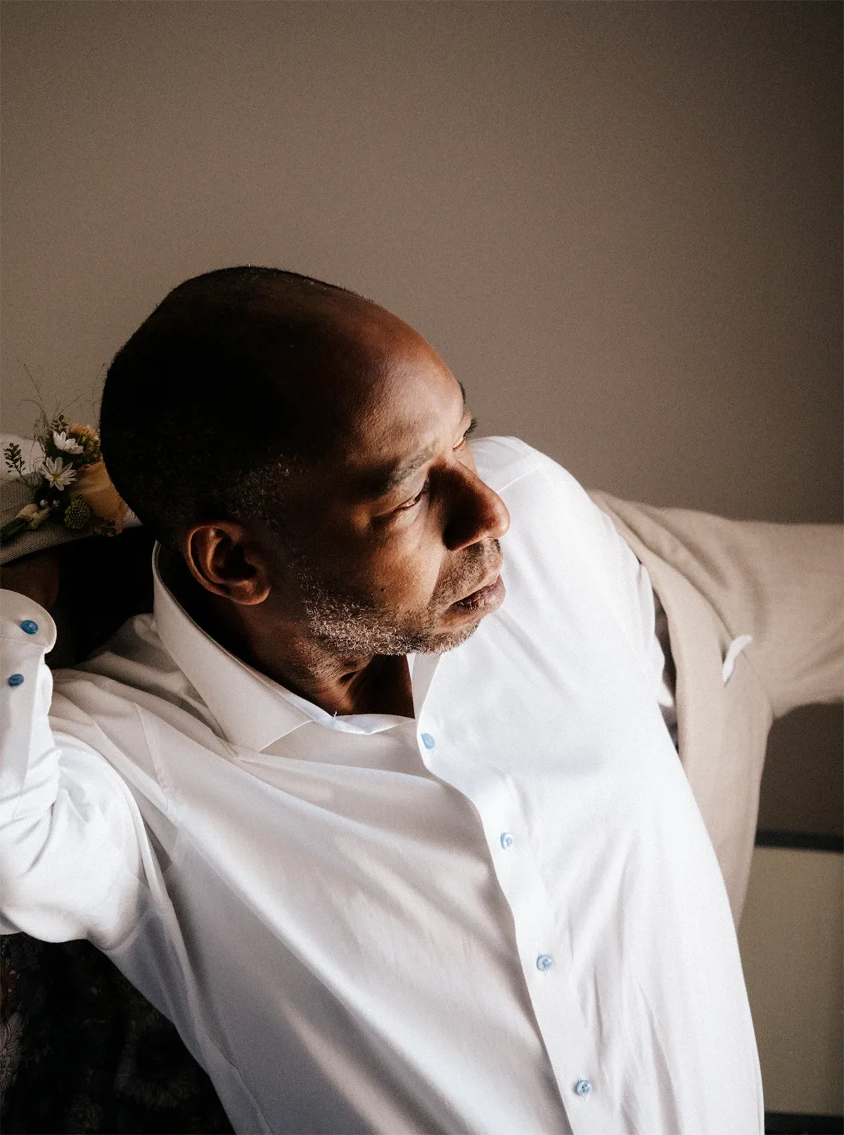 A groom is captured by Muriel Oe Photo, a vendor listed under the wedding photography category at Mariage Elegant, Canada. The image shows the groom in the process of getting ready, wearing a crisp white shirt, as he adjusts his beige suit jacket. The setting appears intimate and well-lit, highlighting the groom's focused expression and attention to detail. This moment is indicative of the essential preparations and emotions leading up to a wedding ceremony, expertly documented by the photographer.