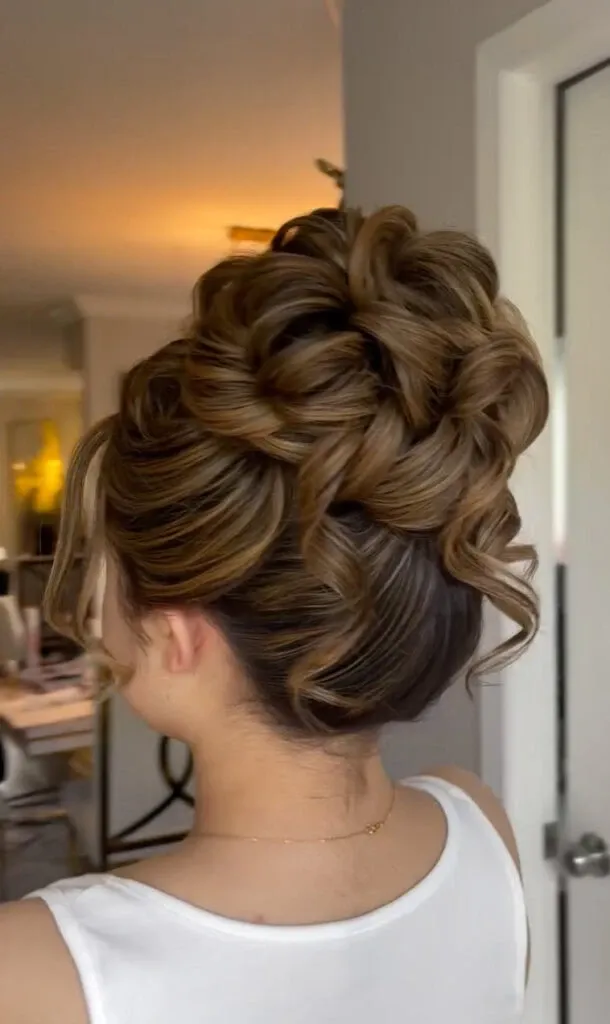 In this elegant image from Mariage MTL, showcased in the Wedding Beauty category on Mariage Elegant, Canada, a bride's hair is styled in an intricate updo. The hairstyle features voluminous, meticulously arranged curls, creating a sophisticated and graceful look perfect for a wedding. The bride is wearing a white sleeveless dress, and the soft lighting enhances the warm tones of the hair. The setting suggests a professional salon environment, emphasizing the expertise and attention to detail provided by Mariage MTL.