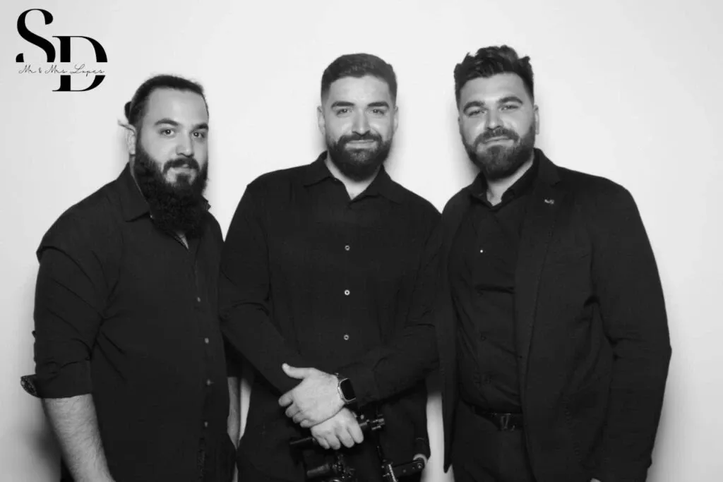 Three men are standing side by side against a plain backdrop, smiling and dressed in dark, formal attire. They are part of PJ Entertainment, a wedding entertainment vendor featured on Mariage Elegant in Canada. One of the men holds a piece of recording equipment, suggesting their role in providing music or sound services for weddings. The image is in black and white, giving it a classic and elegant feel, suitable for the wedding industry context.