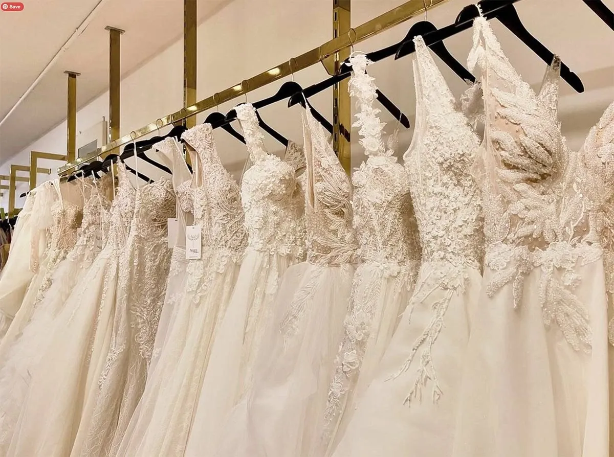 The image showcases a stunning selection of elegant wedding gowns displayed on a gold rack at Maison Mitri, a featured vendor in the Wedding Tuxedo category at Mariage Elegant, Canada. Each gown features intricate lace detailing and luxurious fabrics, reflecting exquisite craftsmanship ideal for brides seeking sophistication for their special day. The setting conveys a sense of classic elegance, highlighting Maison Mitri's dedication to providing high-quality bridal attire.