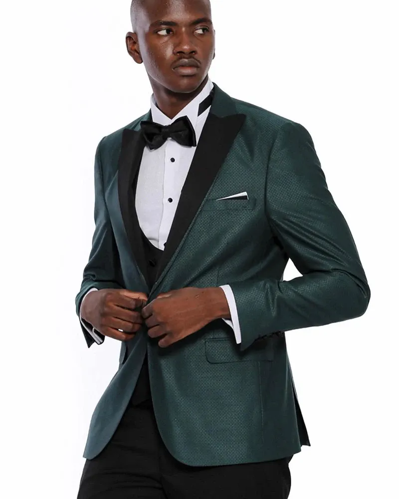 A groom wearing a stylish green tuxedo jacket with black satin lapels, designed by Jaco Uomo, perfect for a wedding. The ensemble includes a crisp white dress shirt, a black bow tie, and matching black dress pants, embodying the elegance and sophistication ideal for a wedding tuxedo. This image showcases the detailed craftsmanship and modern design offered by the Jaco Uomo brand, highlighting its suitability for a memorable matrimonial event.
