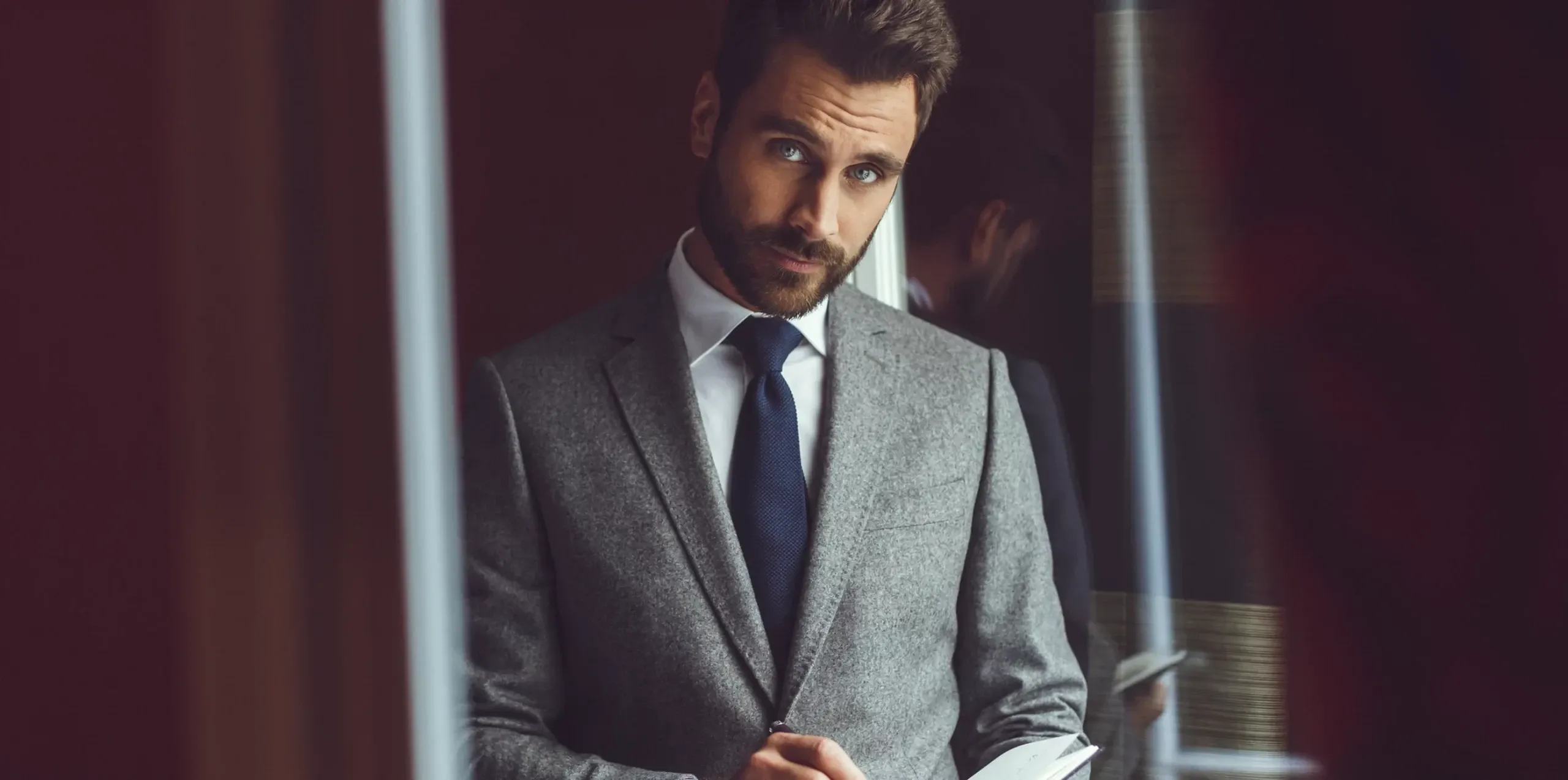 In this image, a well-dressed man is seen wearing a sophisticated grey wedding tuxedo with a crisp white shirt and a dark tie, exemplifying the elegant style offered by Blandin & Delloye. The setting exudes a refined ambiance, suitable for a formal wedding occasion. This visual presentation highlights the vendor's expertise in wedding tuxedos, making it an ideal choice for a stylish and polished wedding look in Canada.