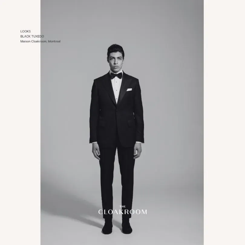 A man is standing in a neutral pose wearing a classic black tuxedo from Maison Cloakroom, specialized in wedding tuxedos. The tuxedo features a well-fitted jacket with a crisp white dress shirt underneath, complemented by a black bow tie and a white pocket square. The overall look is polished and elegant, ideal for a formal wedding setting. The image background is a simple, light gray, drawing attention to the sophisticated attire. Maison Cloakroom is prominently noted, emphasizing its offering for wedding occasions.
