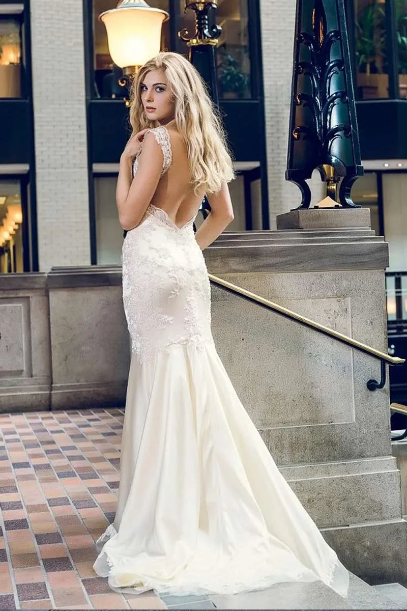 In this image, a bride is elegantly wearing a luxurious wedding dress designed by Charme Atelier, featured in the wedding dress category on Mariage Elegant, Canada. The dress showcases intricate lace detailing on the bodice and delicate cap sleeves, with an alluring open back. The skirt flows gracefully, cascading to the floor with a slight train. The setting is sophisticated, with warm lighting and elegant architecture, enhancing the romantic and refined ambiance perfect for a wedding day.