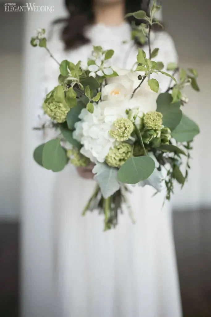 A bride holds an elegant bouquet arranged by Alain Simon Fleurs, showcasing their expertise in wedding floristry. The bouquet features a harmonious blend of white hydrangeas, delicate roses, and lush green foliage, perfectly embodying a natural and sophisticated aesthetic. The intricate floral arrangement highlights the florist's attention to detail, ideal for an elegant wedding setting provided by vendors in the wedding florists category.