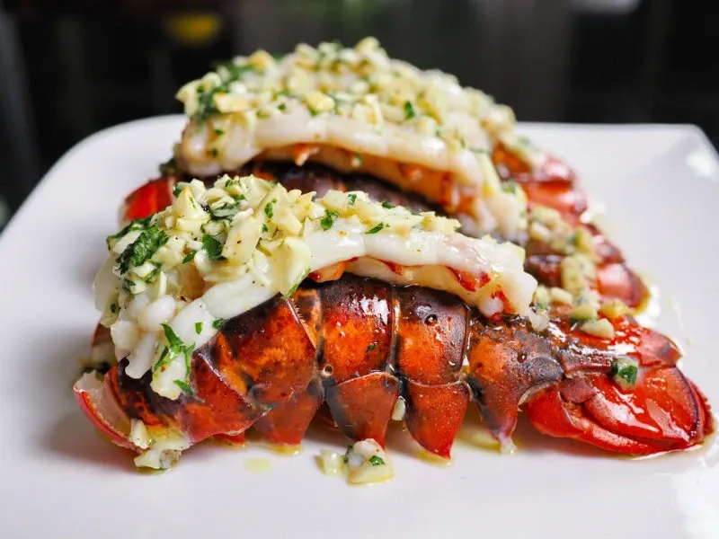A beautifully plated dish of lobster tail topped with a generous amount of seasoned garlic butter sauce garnished with fresh herbs, showcased at Renaissance Centre. This image represents the exquisite catering options available for weddings at this elegant venue, highlighting the venue's attention to gourmet cuisine. Ideal for those seeking a sophisticated dining experience, Renaissance Centre offers remarkable culinary presentations for wedding celebrations in Canada.