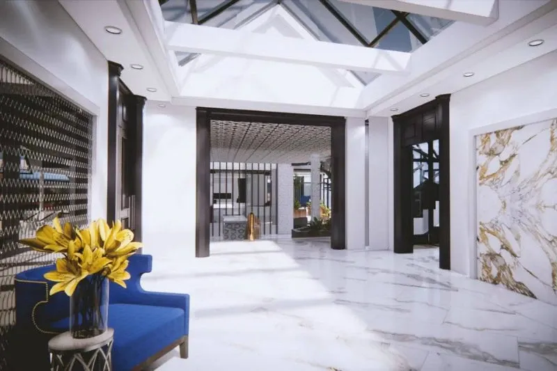 The image showcases the elegant interior of Plaza Le Rizz, a wedding venue listed on Mariage Elegant, Canada. The spacious area features a stunning marble floor and a bright, airy ambiance created by large skylights. A stylish blue chair is positioned to the left, accompanied by a vase of vibrant yellow lilies, adding a touch of color and sophistication. The venue's modern decor is highlighted by the intricate ceiling details and minimalist wall art, providing a luxurious setting perfect for weddings and special events.