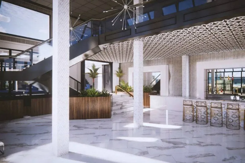 This image showcases the elegant interior of Plaza Le Rizz, a distinguished wedding venue. The spacious room features gleaming white marble floors and sleek white columns that enhance the grandeur of the space. A contemporary staircase with a black railing leads to an upper level, adding depth and sophistication. Overhead, modern chandeliers with starburst designs illuminate the area, complementing the intricate ceiling patterns. The lower level includes a stylish bar area with gold-accented stools, perfect for guests during social gatherings. Lush green plants in wood and white planters add a touch of nature, creating a serene ambiance ideal for weddings.