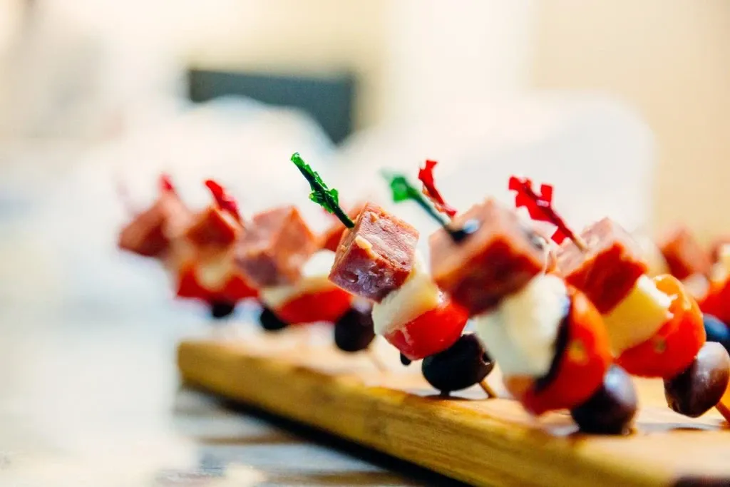 Elegant display of gourmet appetizers on a wooden board at Le St-Martin Hotel & Suites, highlighting the sophisticated catering options available at this wedding venue. The carefully arranged skewers feature an assortment of cubed meats, cheese, cherry tomatoes, and olives, secured with colorful decorative toothpicks, emphasizing the attention to detail and quality that Le St-Martin Hotel & Suites offers for weddings.