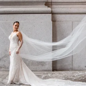 Inhouse Studios Photography, specializing in wedding photography, captures a stunning image of a bride gracefully posing against a grand, stone building. The bride is elegantly dressed in a fitted, lace wedding gown with a long, flowing veil trailing behind her, softly billowing in the breeze. The neutral tones of the stone backdrop enhance the bride's exquisite attire, creating a timeless and sophisticated wedding portrait perfect for Mariage Elegant Canada.