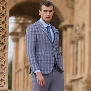 L'image présente un homme portant un élégant smoking de mariage de la marque Baggi, dans un style moderne et raffiné. Le costume, composé d'une veste à carreaux bleus et gris assortie à un pantalon gris clair, est complété par une chemise bleu clair et une cravate bleu foncé. L'homme se tient devant un bâtiment en pierre avec des arches décoratives, ajoutant une touche classique au cadre. Ce smoking de mariage de Baggi est parfait pour les futurs mariés cherchant une tenue chic et sophistiquée.