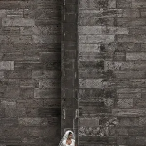 Une mariée en robe blanche élégante se tient contre un mur en pierre imposant, créant un contraste saisissant. Elle porte un voile délicat qui ajoute une touche de douceur à l'atmosphère urbaine et architecturale de la scène. Cette image, capturée par Inhouse Studios Photography, illustre parfaitement l'art de la photographie de mariage, où l'émotion et l'esthétique se rencontrent.
