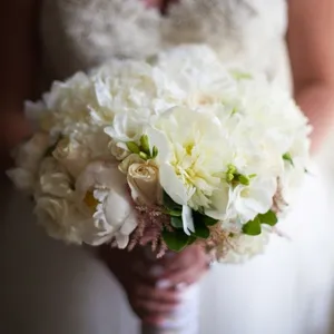 Une mariée tient un bouquet de mariée élégant composé de pivoines blanches et de roses crème, capturé par Inhouse Studios Photography, spécialiste en photographie de mariage. La robe de la mariée, ornée de perles délicates, ajoute une touche sophistiquée à l'image. Le bouquet, avec ses fleurs fraîches et ses nuances douces, reflète un choix classique pour un mariage élégant.