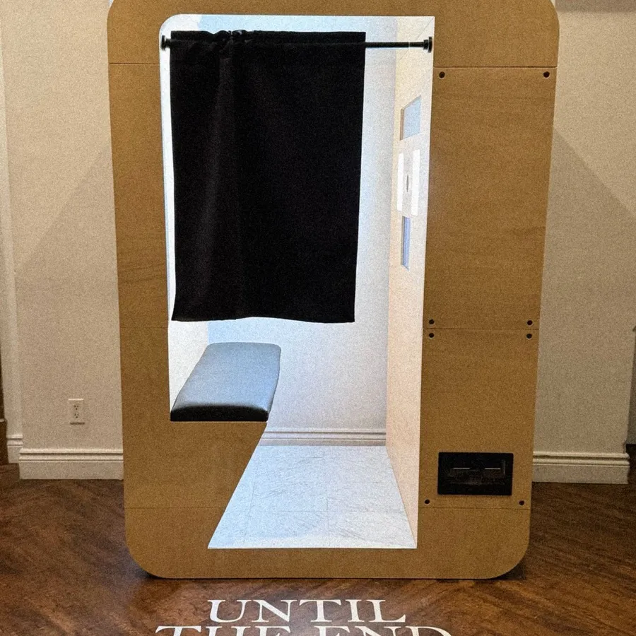 The image features a modern photo booth from Le Fotobooth, categorized under Photo Booth for Mariage Elegant in Canada. The booth has a sleek wooden frame with a black curtain that can be drawn for privacy, ideal for capturing intimate wedding moments. Inside, there is a comfortable bench seat for guests to sit on while taking photos. The floor in front of the booth has the romantic phrase 