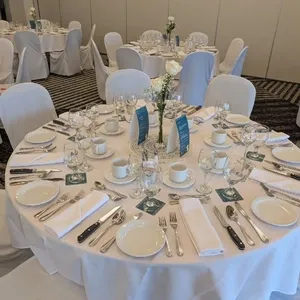 Salle de réception élégante du Doubletree par Hilton Québec Resort, mettant en avant une table de banquet rondement dressée pour un mariage. Les tables sont couvertes de nappes blanches immaculées et entourées de chaises assorties. La vaisselle est soigneusement disposée, avec des couverts brillants et de la verrerie raffinée. Chaque table est ornée d’un centre de table floral simple, accentuant la sophistication de l'espace prête pour une cérémonie nuptiale. Ambiance lumineuse et décoration soignée, idéale pour célébrations de mariage.