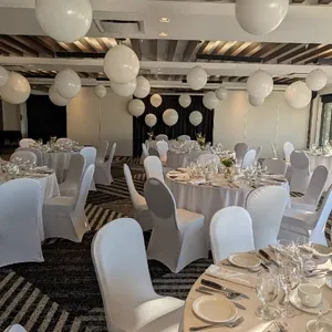 La salle de réception du Doubletree par Hilton Québec Resort est décorée pour un mariage raffiné. On y voit des tables rondes élégamment dressées avec des nappes blanches et des chaises assorties. Les tables sont ornées de bouquets floraux délicats en leur centre, et des ballons blancs flottent au plafond, ajoutant une touche festive. La lumière naturelle entre par de grandes fenêtres, illuminant la pièce. Cet espace moderne et accueillant est idéal pour célébrer des noces mémorables.