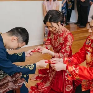 Dans cette image, deux couples portent des tenues de mariage traditionnelles chinoises richement décorées. La mariée et le marié, assis au centre, échangent des enveloppes rouges, symboles de chance et de bonheur, avec leurs aînés. Les vêtements sont ornés de motifs dorés et rouges éclatants, typiques des célébrations de mariage asiatiques. Les invités en arrière-plan observent la cérémonie avec attention. Cette scène représente un moment culturel important dans les mariages. KNL Productions, spécialisé dans l'animation, capture cet événement précieux pour Mariage Elegant au Canada, ajoutant une touche authentique et festive à la célébration.