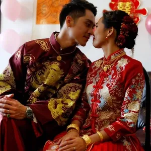 Dans cette image de Mariage Elegant, Canada, deux personnes vêtues de tenues de mariage traditionnelles chinoises sont assises côte à côte. L'homme porte un costume rouge orné de motifs dorés de dragons, symbole de puissance et de chance. La femme porte une robe rouge richement décorée avec des détails dorés et des motifs floraux. Ils sont assis dans un décor intérieur avec des ballons roses et des décorations murales, créant une atmosphère joyeuse et festive. Ce moment capturé représente l'élégance et le respect des traditions lors d'une cérémonie de mariage. Dans le cadre de l'animation de mariage offerte par KNL Productions, cette scène illustre comment les traditions culturelles peuvent être intégrées dans les festivités modernes.