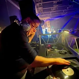 Dans cette image, un DJ de Productions Megamix anime une soirée de mariage. Le DJ, portant un casque audio, est concentré sur son plateau de mixage où il manipule des vinyles. L'éclairage d'ambiance crée une atmosphère festive et moderne, idéale pour une réception de mariage animée. Ce cadre professionnel met en valeur l'expertise de la catégorie Animation de Productions Megamix, spécialisée dans les événements élégants et dynamiques au Canada.