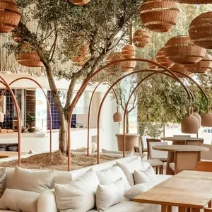 L'image montre un magnifique espace de réception intérieure avec un thème naturel et élégant, proposé par le prestataire Voyage Club Evasion dans la catégorie Mariage à destination. La salle est décorée avec des paniers en osier suspendus et un arbre central entouré de sièges confortables et de tables en bois clair. Les baies vitrées offrent une vue imprenable sur une marina pittoresque, ajoutant une touche de charme maritime à l'ambiance. Cet environnement offre un cadre idéal pour un mariage sophistiqué et mémorable.