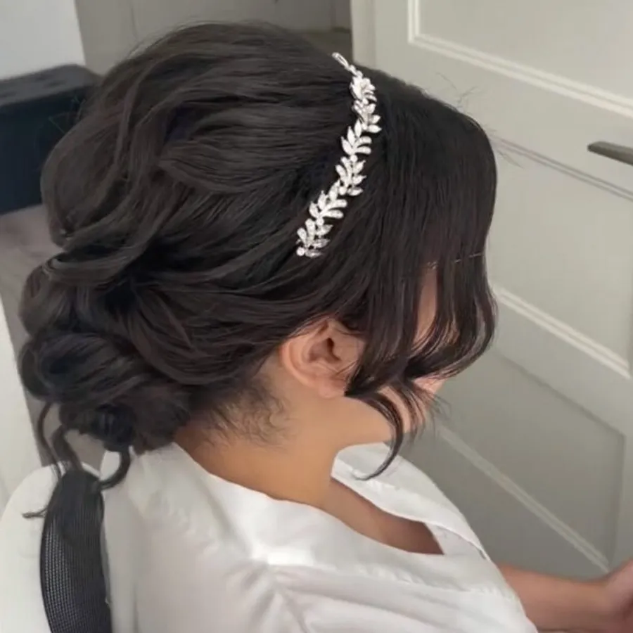 Dans cette image, une mariée est assise de profil, mettant en valeur une coiffure de mariage élégante réalisée par le fournisseur Mariage MTL, classé dans la catégorie Beauté pour le mariage. Ses cheveux bruns sont coiffés en un chignon complexe et sophistiqué, orné d