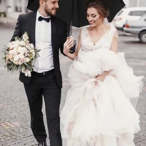 gorgeous bride and stylish groom walking under umbrella in rainy street and smiling